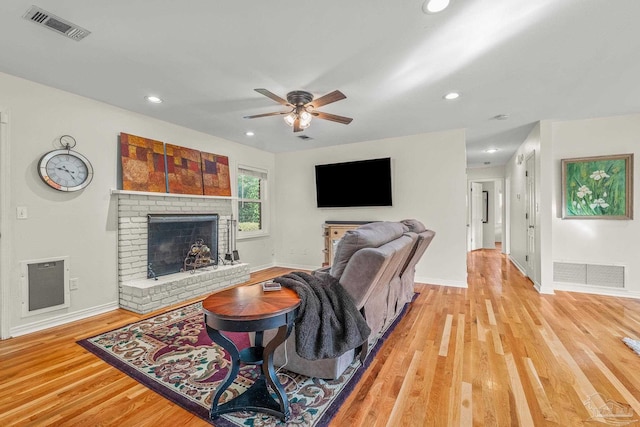 living room featuring ceiling fan, light wood-type flooring, and a fireplace