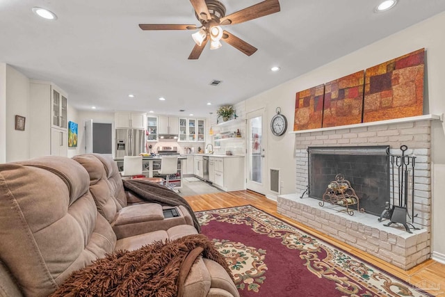 living room featuring ceiling fan, light hardwood / wood-style floors, and a brick fireplace