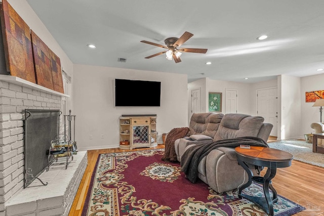 living room featuring ceiling fan, a fireplace, and light hardwood / wood-style flooring