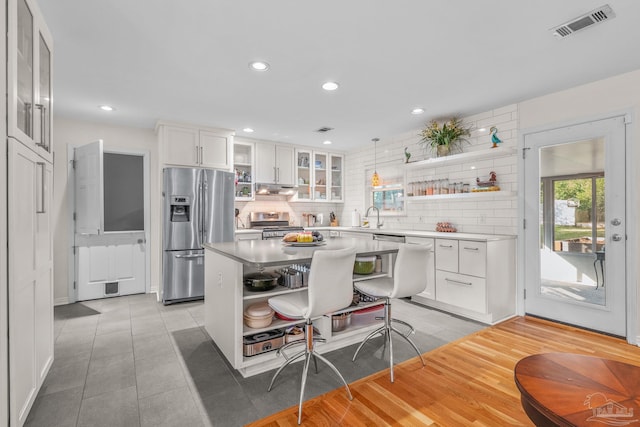 kitchen with appliances with stainless steel finishes, white cabinetry, hanging light fixtures, a center island, and decorative backsplash