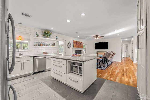 kitchen with stainless steel appliances, tasteful backsplash, white cabinets, a kitchen island, and decorative light fixtures