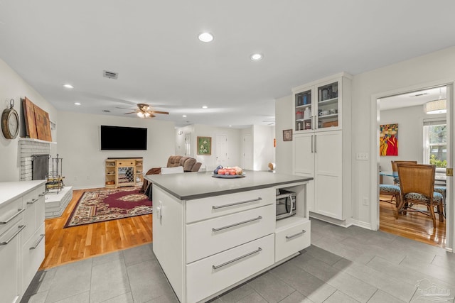 kitchen featuring white cabinets, a center island, light tile patterned floors, ceiling fan, and a brick fireplace