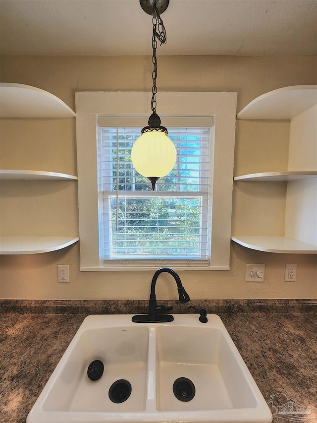 kitchen featuring dark countertops, pendant lighting, open shelves, and a sink