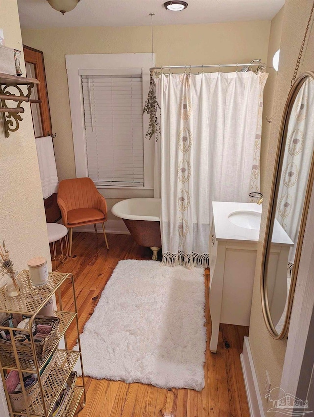 bathroom featuring a freestanding bath, a shower with shower curtain, wood finished floors, and vanity