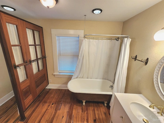 bathroom featuring a tub to relax in, curtained shower, wood finished floors, vanity, and baseboards