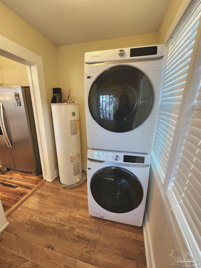 laundry room with water heater, a textured ceiling, wood finished floors, and stacked washer / drying machine