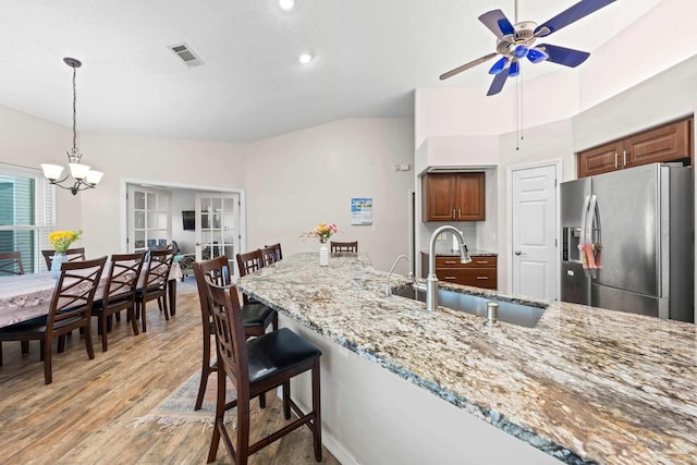 kitchen with light hardwood / wood-style floors, sink, ceiling fan with notable chandelier, stainless steel refrigerator with ice dispenser, and light stone countertops