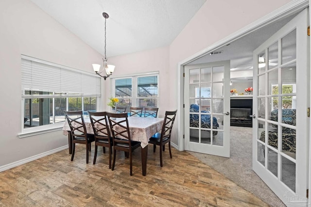 dining room with wood-type flooring, a textured ceiling, lofted ceiling, and a chandelier