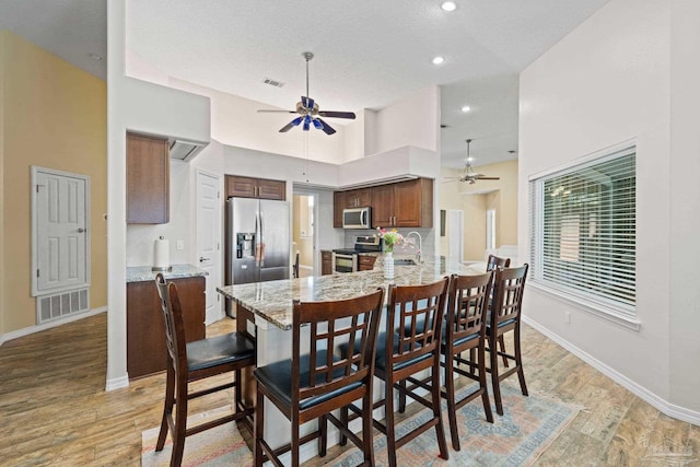 dining room featuring a textured ceiling, a high ceiling, ceiling fan, light hardwood / wood-style flooring, and sink