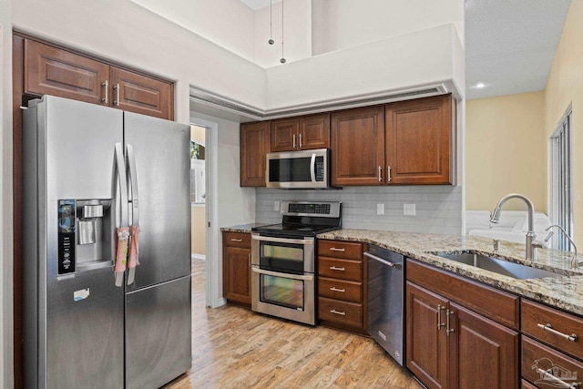 kitchen with light wood-type flooring, sink, backsplash, appliances with stainless steel finishes, and light stone countertops