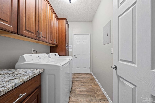 clothes washing area with electric panel, washing machine and clothes dryer, a textured ceiling, cabinets, and hardwood / wood-style flooring