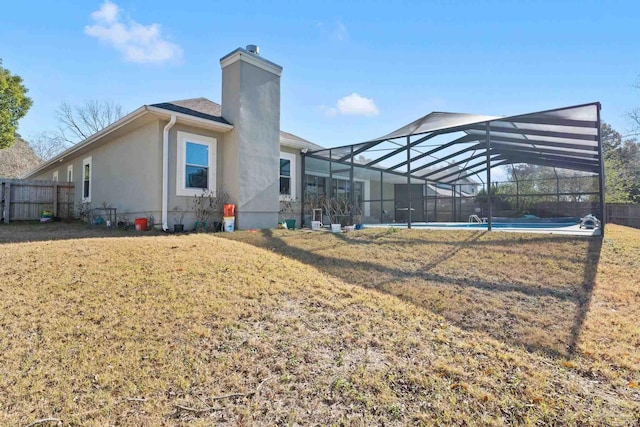 back of property with glass enclosure, a yard, and a fenced in pool