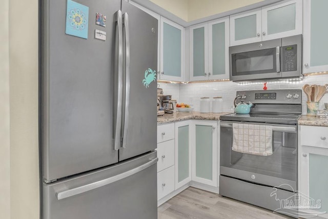10443 Gulf Beach Hwy Unit 1, Pensacola, FL 32507 - kitchen featuring backsplash, light wood finished floors, white cabinets, light stone countertops, and appliances with stainless steel finishes