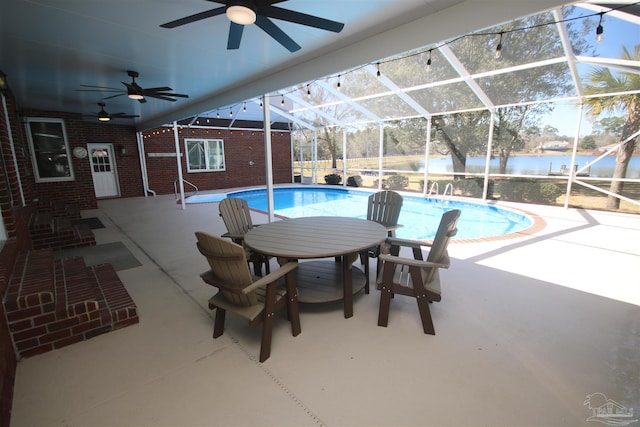 outdoor pool with ceiling fan, a patio, a water view, and a lanai