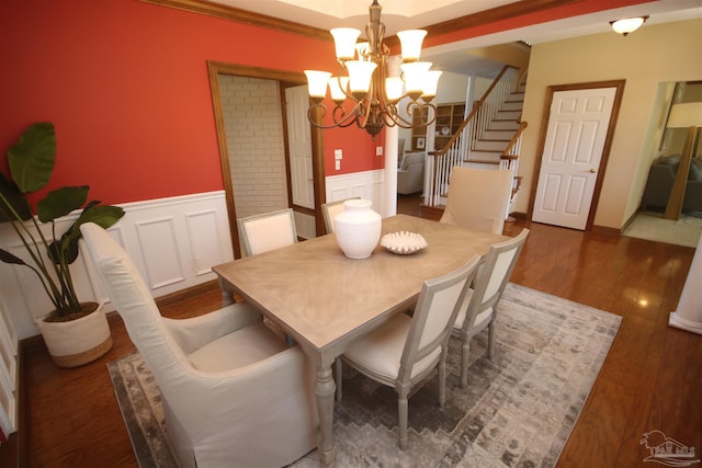 dining room with a wainscoted wall, stairs, wood finished floors, and an inviting chandelier