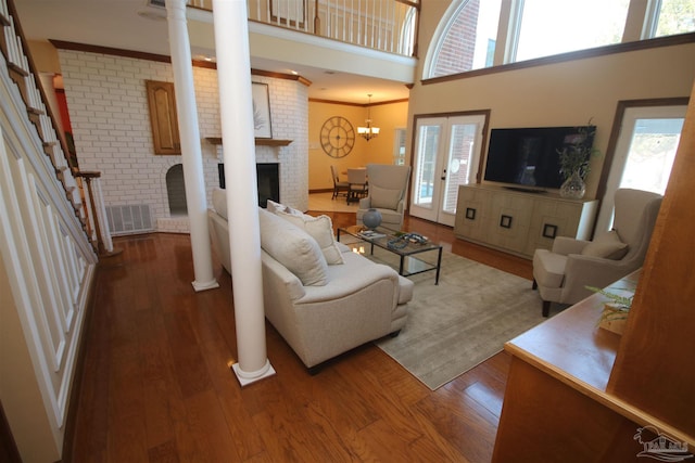 living area with a high ceiling, stairway, a brick fireplace, dark wood-style floors, and ornate columns