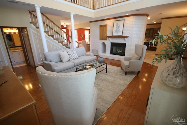 living room featuring a fireplace, wood finished floors, ornamental molding, stairway, and decorative columns