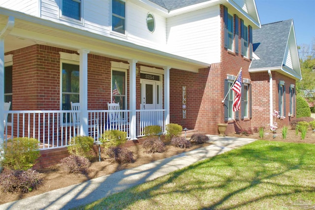 view of front of home featuring covered porch, roof with shingles, and brick siding