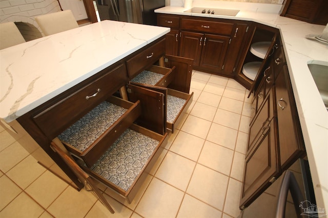 kitchen featuring light tile patterned floors, light stone counters, black electric cooktop, refrigerator, and dark brown cabinets