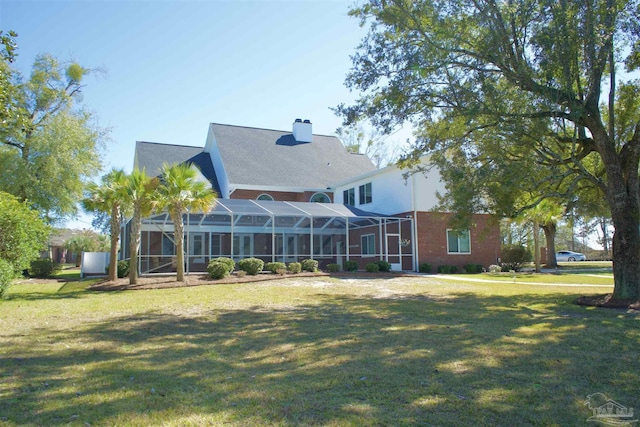 back of property with a yard, a chimney, and a lanai