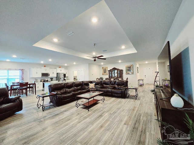 living room with light wood-style floors, visible vents, a raised ceiling, and recessed lighting