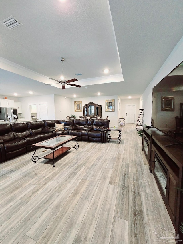 living room featuring recessed lighting, a ceiling fan, visible vents, light wood-type flooring, and a tray ceiling