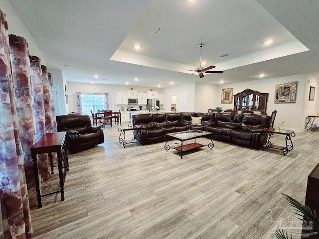 living area with light wood finished floors, visible vents, a raised ceiling, crown molding, and recessed lighting