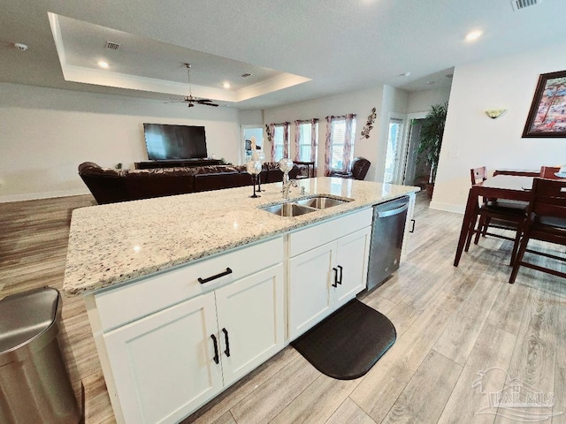 kitchen with light wood finished floors, a raised ceiling, a sink, light stone countertops, and dishwasher