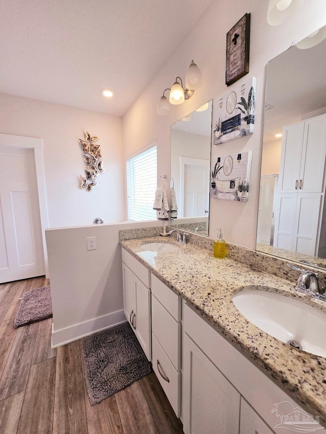 bathroom with double vanity, baseboards, a sink, and wood finished floors