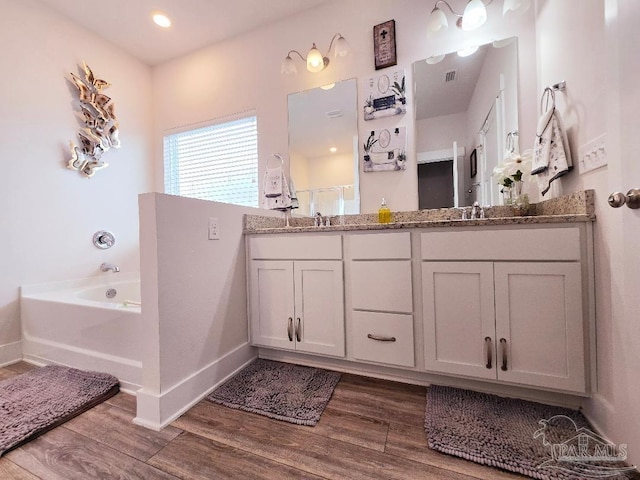 full bath with a garden tub, double vanity, a sink, wood finished floors, and baseboards