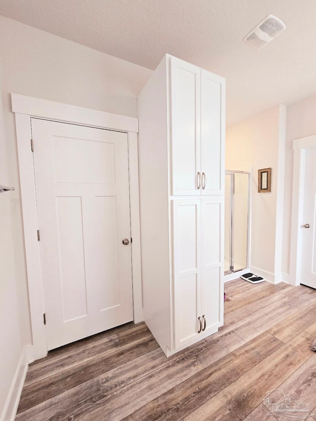 hallway featuring light wood-style flooring, visible vents, and baseboards