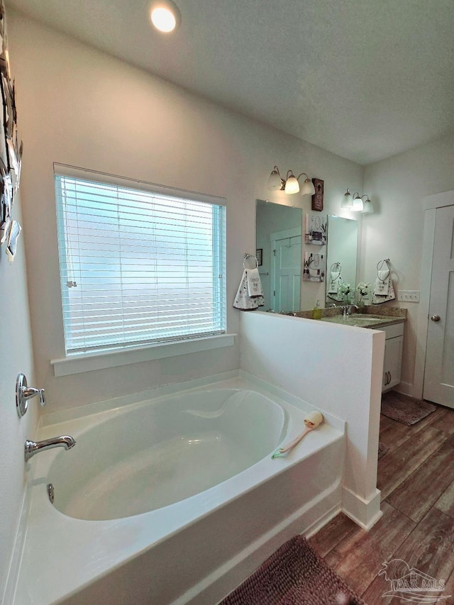 bathroom with wood finished floors, vanity, a textured ceiling, and a bath