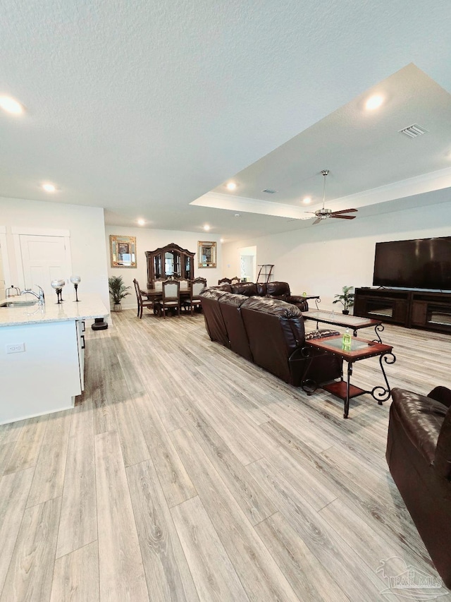 living room with a textured ceiling, recessed lighting, visible vents, light wood finished floors, and a raised ceiling