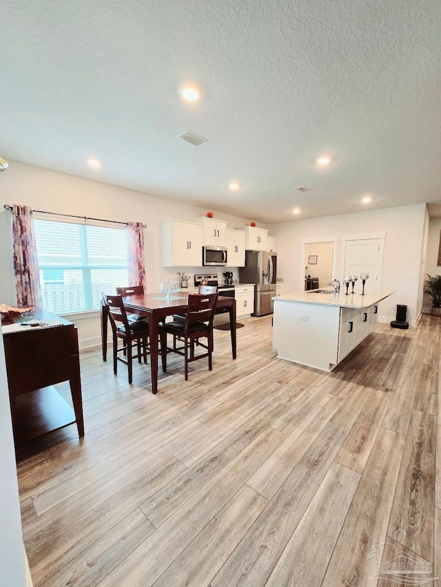 dining space featuring light wood finished floors, visible vents, a textured ceiling, and recessed lighting