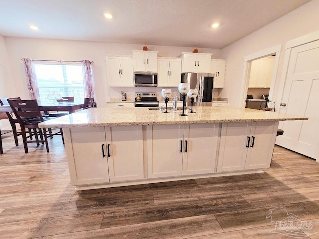 kitchen with stainless steel appliances, white cabinetry, a sink, wood finished floors, and a large island with sink