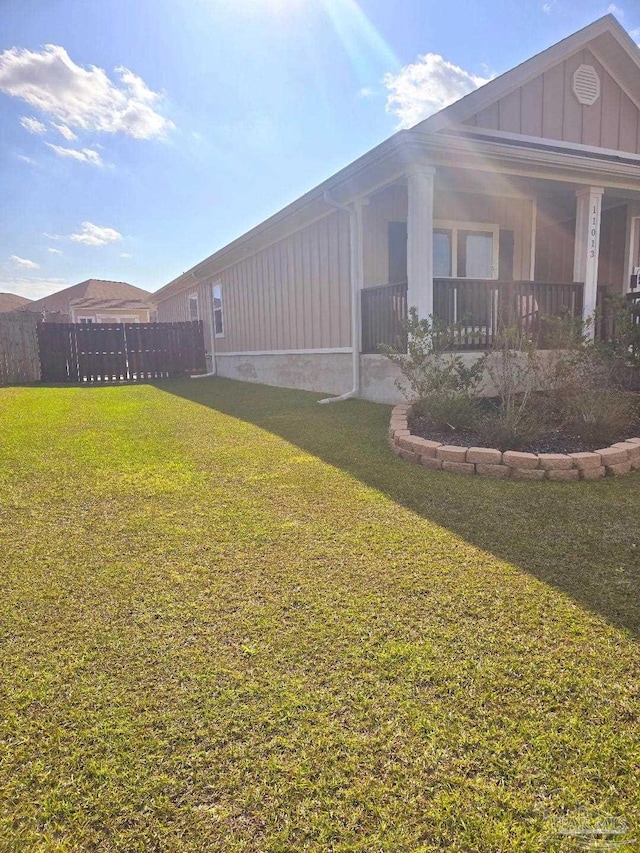 view of side of home featuring a yard, a porch, board and batten siding, and fence