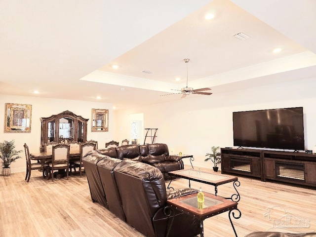 living area with light wood finished floors, visible vents, a raised ceiling, and recessed lighting