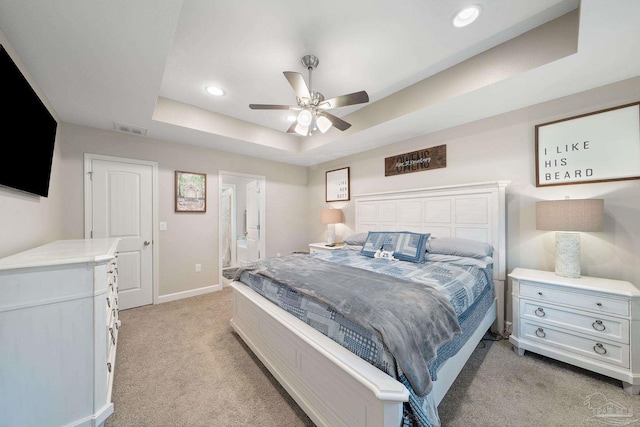 bedroom with ceiling fan, ensuite bathroom, a tray ceiling, and light colored carpet