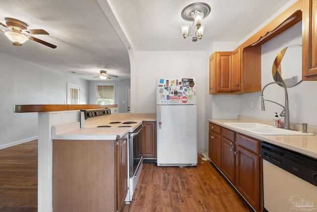 kitchen with dark wood-type flooring, kitchen peninsula, a notable chandelier, sink, and white appliances