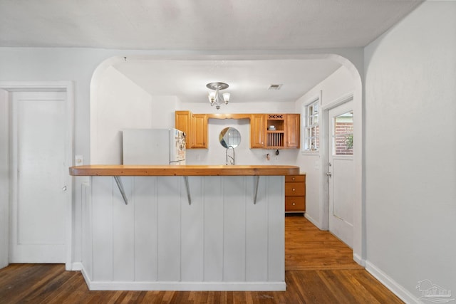 kitchen with kitchen peninsula, a notable chandelier, dark hardwood / wood-style floors, white fridge, and a breakfast bar