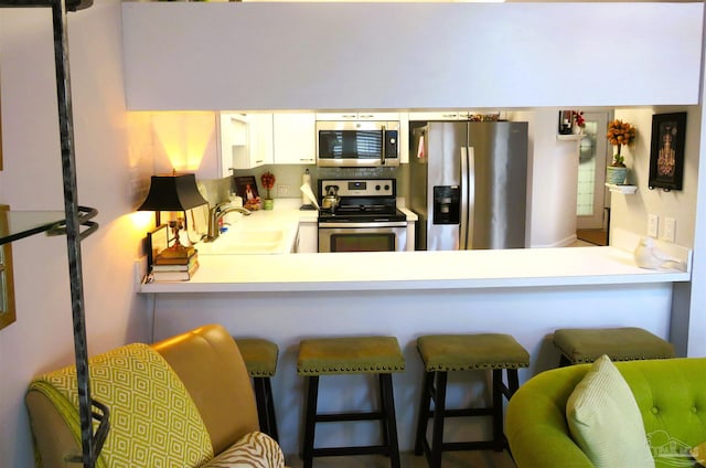 kitchen featuring white cabinetry, sink, a kitchen bar, kitchen peninsula, and stainless steel appliances