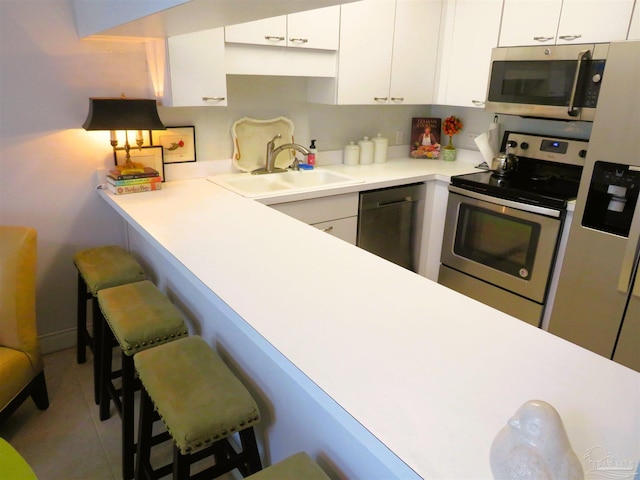 kitchen with sink, a breakfast bar area, white cabinetry, light tile patterned floors, and stainless steel appliances