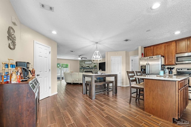 kitchen with ceiling fan, a kitchen island, pendant lighting, appliances with stainless steel finishes, and light stone counters