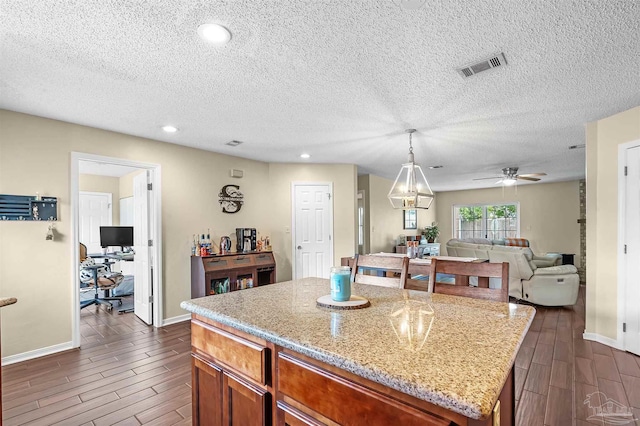 kitchen with a textured ceiling, ceiling fan, a kitchen island, and light stone counters