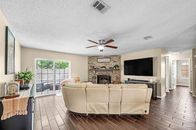 living room featuring a textured ceiling, a brick fireplace, and ceiling fan