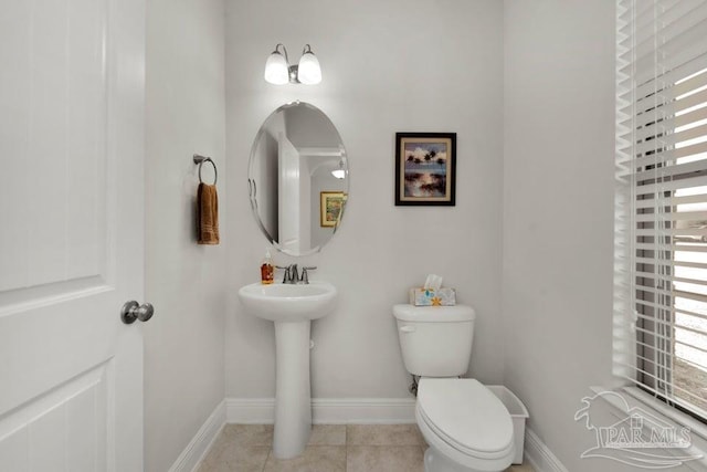 half bathroom featuring baseboards, a sink, toilet, and tile patterned floors