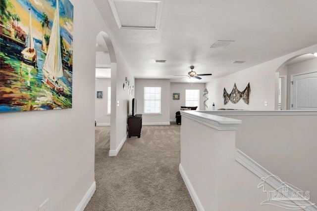 hall featuring light carpet, attic access, baseboards, arched walkways, and an upstairs landing