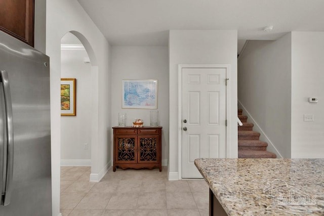 kitchen featuring light tile patterned floors, baseboards, arched walkways, light stone counters, and freestanding refrigerator