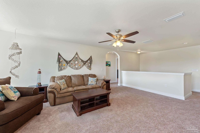 living room featuring arched walkways, ceiling fan, a textured ceiling, light carpet, and visible vents