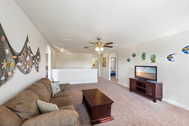 living area with baseboards, arched walkways, ceiling fan, and light colored carpet